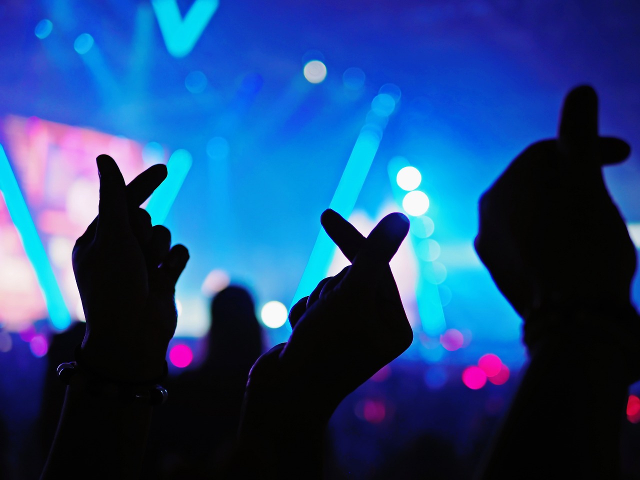 Imagen de manos de personas en un concierto con una señal de cariño coreana