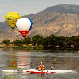 Una persona navega en una canoa blanca sobre la Laguna Caren, mientras dos globos aerostáticos de colores vuelan cerca de los cerros durante el Tiny Fest.