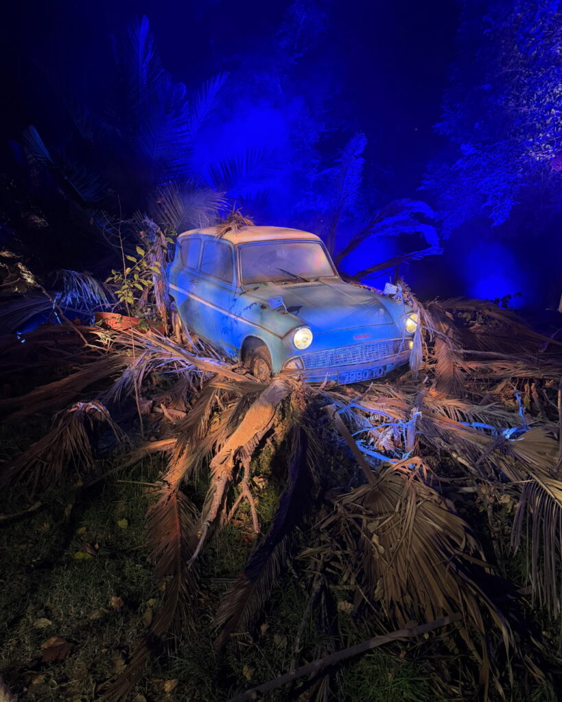  Un auto clásico de color azul rodeado de ramas secas y palmeras bajo una intensa iluminación azul, recreando una escena mágica en el Parque Quinta Normal.