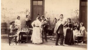 Fotografía histórica que captura el momento en que un vendedor a caballo entrega productos a una mujer y sus hijos frente a una casa de fachada continua. Esta escena refleja la importancia de los oficios chilenos antiguos en el abastecimiento y la vida urbana de los barrios de antaño.