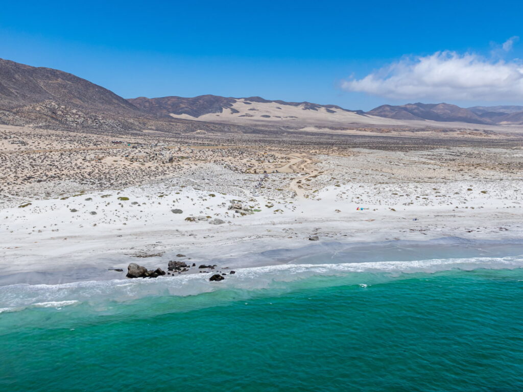 Vista panorámica aérea de la costa del Parque Nacional Llanos de Challe, mostrando una playa de arenas blancas, un mar de color verde intenso y llanuras áridas.