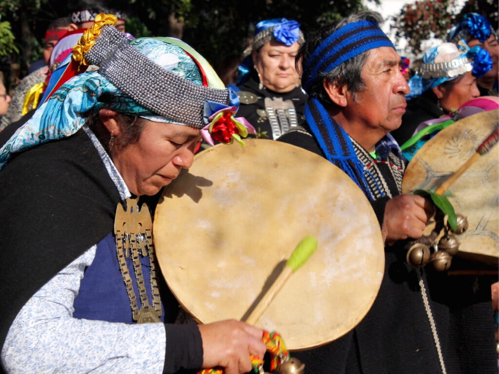 Hombres y mujeres del pueblo mapuche con vestimentas y platería tradicional tocando el kultrún con devoción durante la ceremonia del We Tripantu.