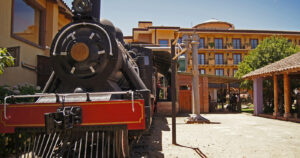 Una histórica locomotora de vapor de color negro con detalles rojos está en exhibición junto a un andén, formando parte del circuito del Museo de Colchagua en Santa Cruz, uno de los atractivos panoramas bajo techo en Chile. Al fondo se observa el edificio de estilo colonial del museo bajo un cielo despejado.