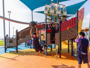 Niños jugando en un colorido juego infantil con forma de barco pirata frente al mar, en un parque costero de Antofagasta, uno de los panoramas para el Día del Niño en Chile.