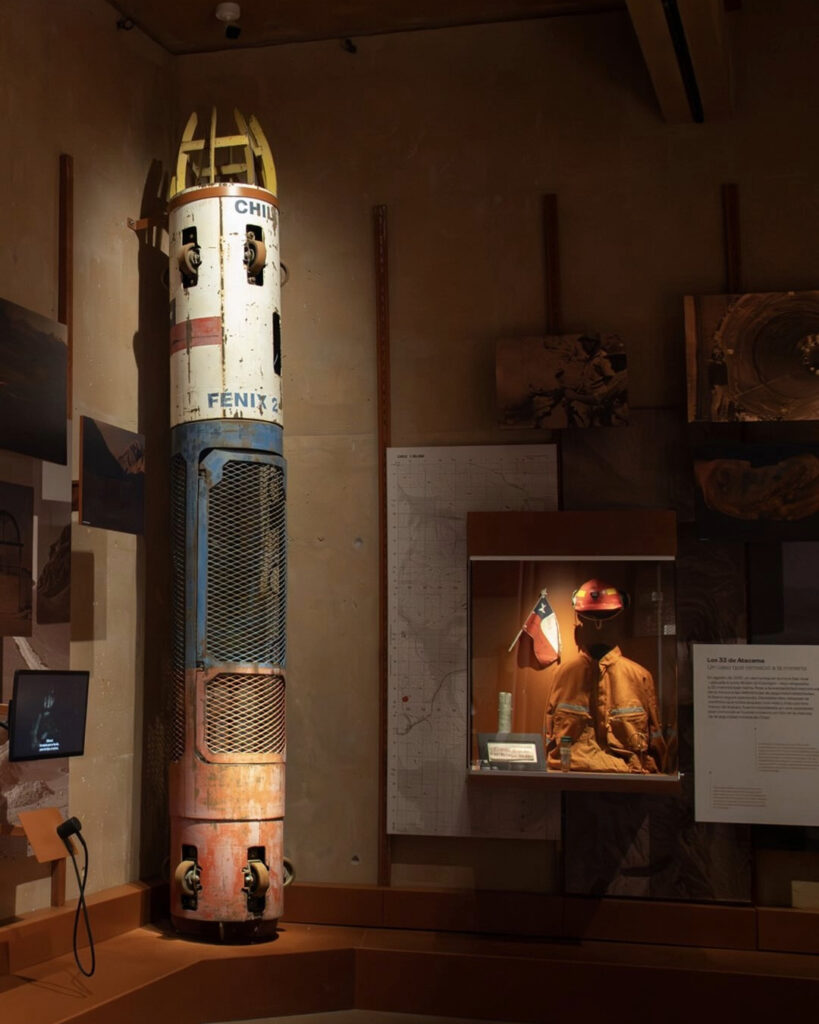 La cápsula de rescate Fénix 2 en exhibición dentro de una sala del Museo Regional de Atacama, acompañada de vitrinas con implementos de minería. 