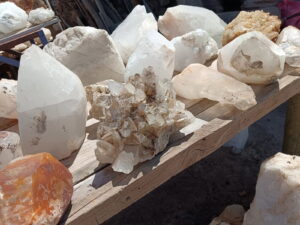 Una colección de grandes formaciones de cristales de cuarzo blanco se exhiben sobre una mesa rústica de madera al aire libre en Quilimarí. Es una parada característica de la artesanía geológica incluida en los panoramas bajo techo en Chile.