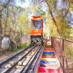 Ascensor tipo funicular de colores vivos recorriendo su vía entre árboles en el Parque de la Infancia de Recoleta, Santiago.