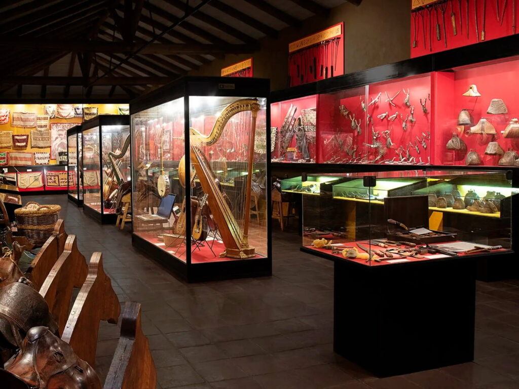 Exposición interior del Museo Colchagua en Santa Cruz con grandes vitrinas iluminadas que exhiben instrumentos musicales típicos como arpas y guitarras, además de espuelas y aperos tradicionales de huaso. 