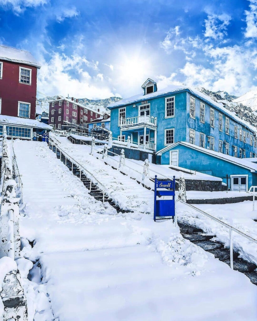  Vista de las coloridas edificaciones de madera azul y roja en el campamento minero de Sewell cubierto por una capa gruesa de nieve invernal, con sus clásicas escaleras centrales nevadas. 