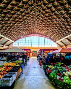 Interior del Mercado Municipal de Cauquenes mostrando un pasillo central limpio con locales comerciales llenos de frutas, verduras y productos locales a ambos lados.
