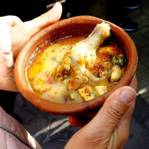 Primer plano de unas manos sosteniendo un pocillo de greda con un caldillo marino caliente, donde se aprecia un trozo de pescado, mariscos y un toque de ají color, característico de la Feria de los Caldos.