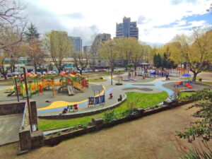 Juegos infantiles junto a áreas verdes y edificios de fondo en el Parque Ecuador de Concepción, el "pulmón verde" penquista, ideal para el Día del Niño.