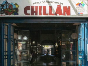 Acceso principal al tradicional Mercado Municipal de Chillán bajo un gran letrero que lleva su nombre en letras rojas, un espacio ideal para buscar artesanías y panoramas bajo techo en Chile. Al fondo se observa el pasillo interior con puestos comerciales abiertos.