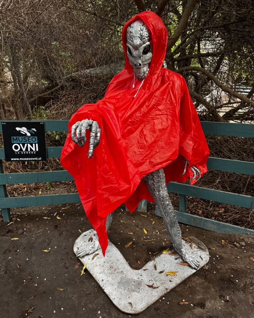 Figura de un extraterrestre gris con capa roja junto al letrero del Museo OVNI en La Serena, ubicada en el sector exterior del recinto rodeado de vegetación