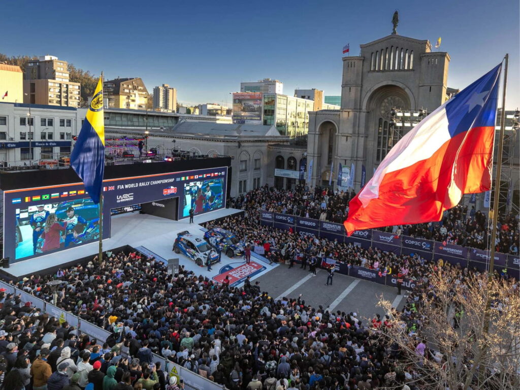  Multitud reunida en la Plaza de la Independencia de Concepción durante la ceremonia de partida del Rally Biobío 2026, con pantallas gigantes, autos de competencia y la bandera chilena ondeando.