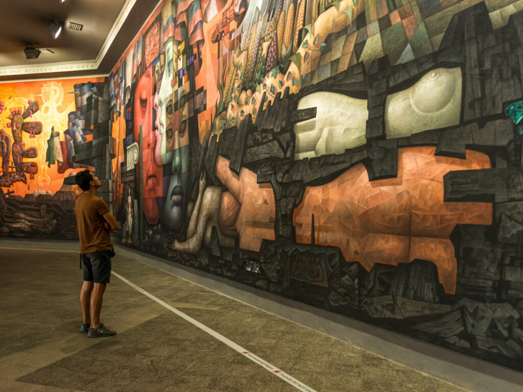 Visitante contemplando el mural "Presencia de América Latina" en la Universidad de Concepción, con sus figuras cubistas de colores intensos, uno de los atractivos culturales para complementar la visita al Rally Biobío 2026. 