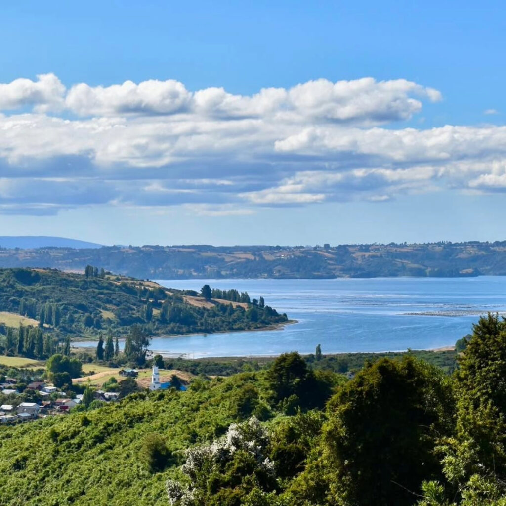 Panorámica desde la Península de Rilán hacia el mar interior de Chiloé, con una iglesia de madera asomando entre el verdor de los campos y humedales.