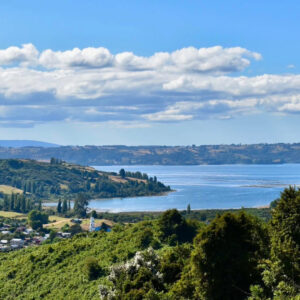 Panorámica desde la Península de Rilán hacia el mar interior de Chiloé, con una iglesia de madera asomando entre el verdor de los campos y humedales.