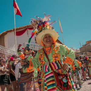 Bailarina luce un vistoso traje tradicional con tocado de plumas y colores vivos, en medio del confeti y las banderas chilenas durante una celebración religiosa del norte del país.