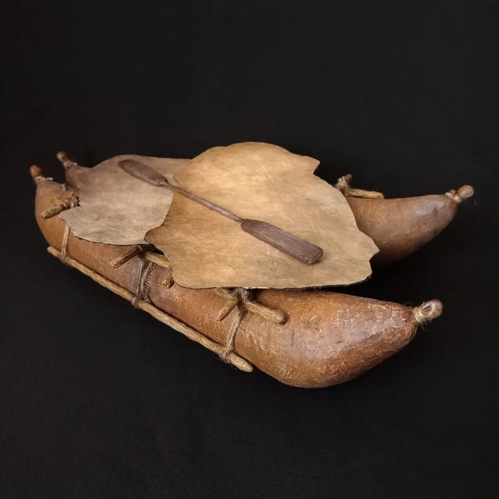 Réplica de una balsa de cuero de lobo marino del pueblo Chango, con remo de madera, sobre fondo negro.