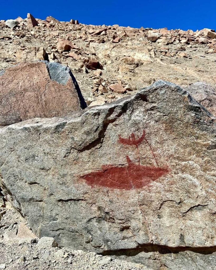 Pintura rupestre en tonos rojos sobre una roca, con la figura de una balsa y un pescador, arte asociado al pueblo Chango.