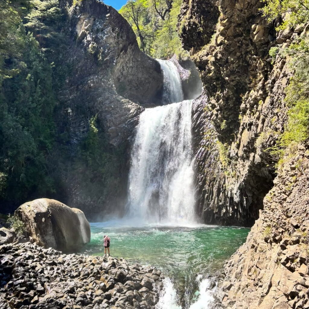 Una cascada se precipita entre paredes de roca volcánica hacia una poza turquesa, en el Parque Peumayen Tenglo, uno de los tesoros escondidos de Chile ideales para el trekking.