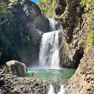 Una cascada se precipita entre paredes de roca volcánica hacia una poza turquesa, en el Parque Peumayen Tenglo, uno de los tesoros escondidos de Chile ideales para el trekking.