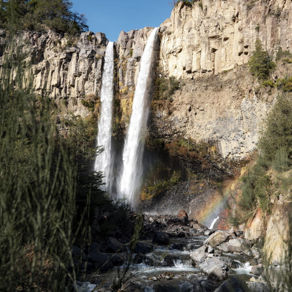 Dos caídas de agua se precipitan desde un muro rocoso formando un arcoíris en su base, en uno de los paisajes cordilleranos que la primavera en Chile revive con el aumento del caudal en el Parque Nacional Laguna del Laja.