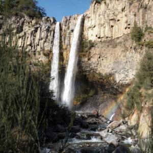 Dos caídas de agua se precipitan desde un muro rocoso formando un arcoíris en su base, en uno de los paisajes cordilleranos que la primavera en Chile revive con el aumento del caudal en el Parque Nacional Laguna del Laja.