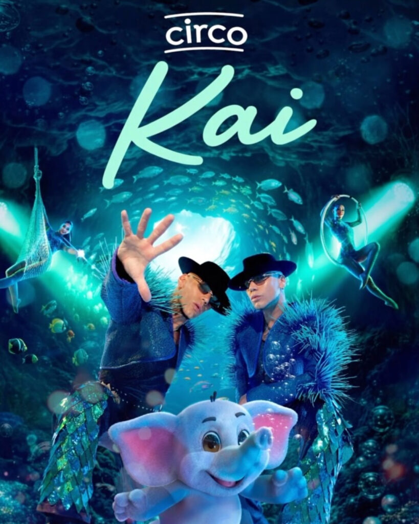 afiche de Circo Kai, con dos artistas con sombreros negros y trajes azules con plumas, un elefante celeste de fantasía y acróbatas en un escenario submarino