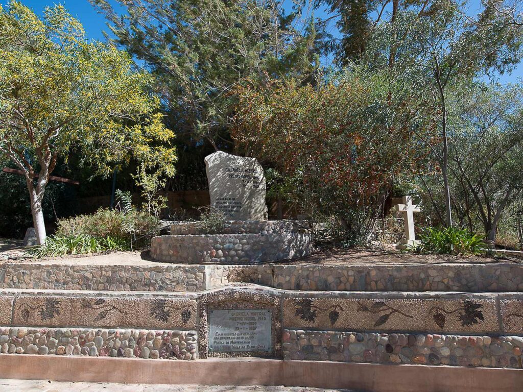 Tumba de Gabriela Mistral en Montegrande, Valle de Elqui, región de Coquimbo. Es una piedra con el nombre de la poeta y la mención al Premio Nobel 1945, rodeada de árboles y muros de piedra de río con mosaicos de racimos de uva.