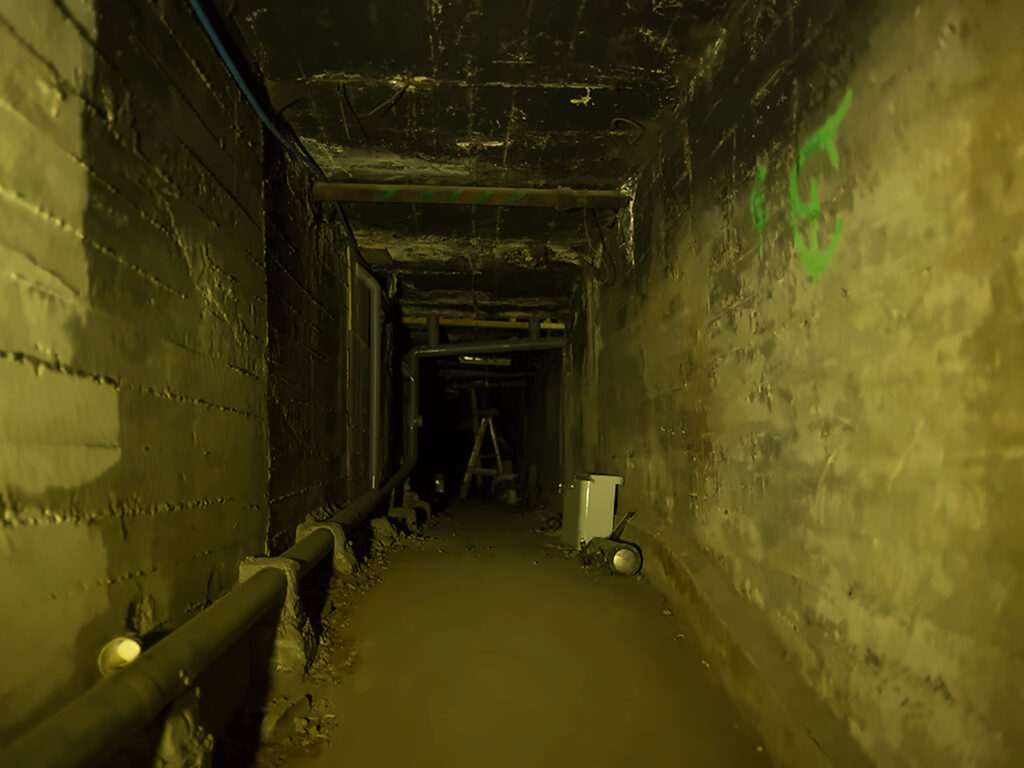 Túnel subterráneo de muros de piedra con tuberías y luz tenue, un recorrido de ambiente misterioso entre los panoramas para Halloween 2026 en Santiago. 