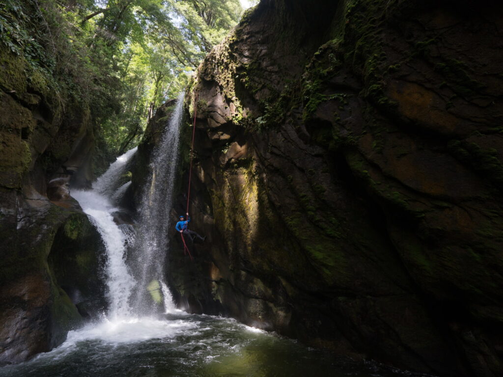 Persona descendiendo en rápel junto a una cascada en un cañón cubierto de musgo, practicando canyoning en Pucón.