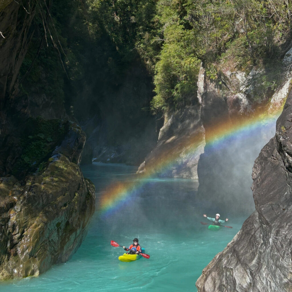  Dos kayakistas remando en aguas turquesa entre paredes de roca, con un arcoíris sobre el río, en Chile 