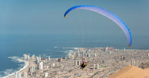 Parapente biplaza con vela azul sobrevolando Iquique, con la duna, la playa y el océano Pacífico al fondo, en Chile, nominado a Mejor Destino de Turismo Aventura en los World Travel Awards 2026.